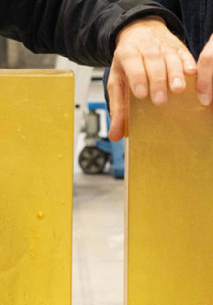 Cette photo a été prise par Boris Dunand au Musée Ariana et représente deux briques de verre jaune tenues à la verticale par deux hommes habillés en noir, dont on ne voit que les mains et le pull.