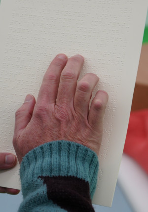 Cette photo représente une main en gros plan qui lit une page de braille