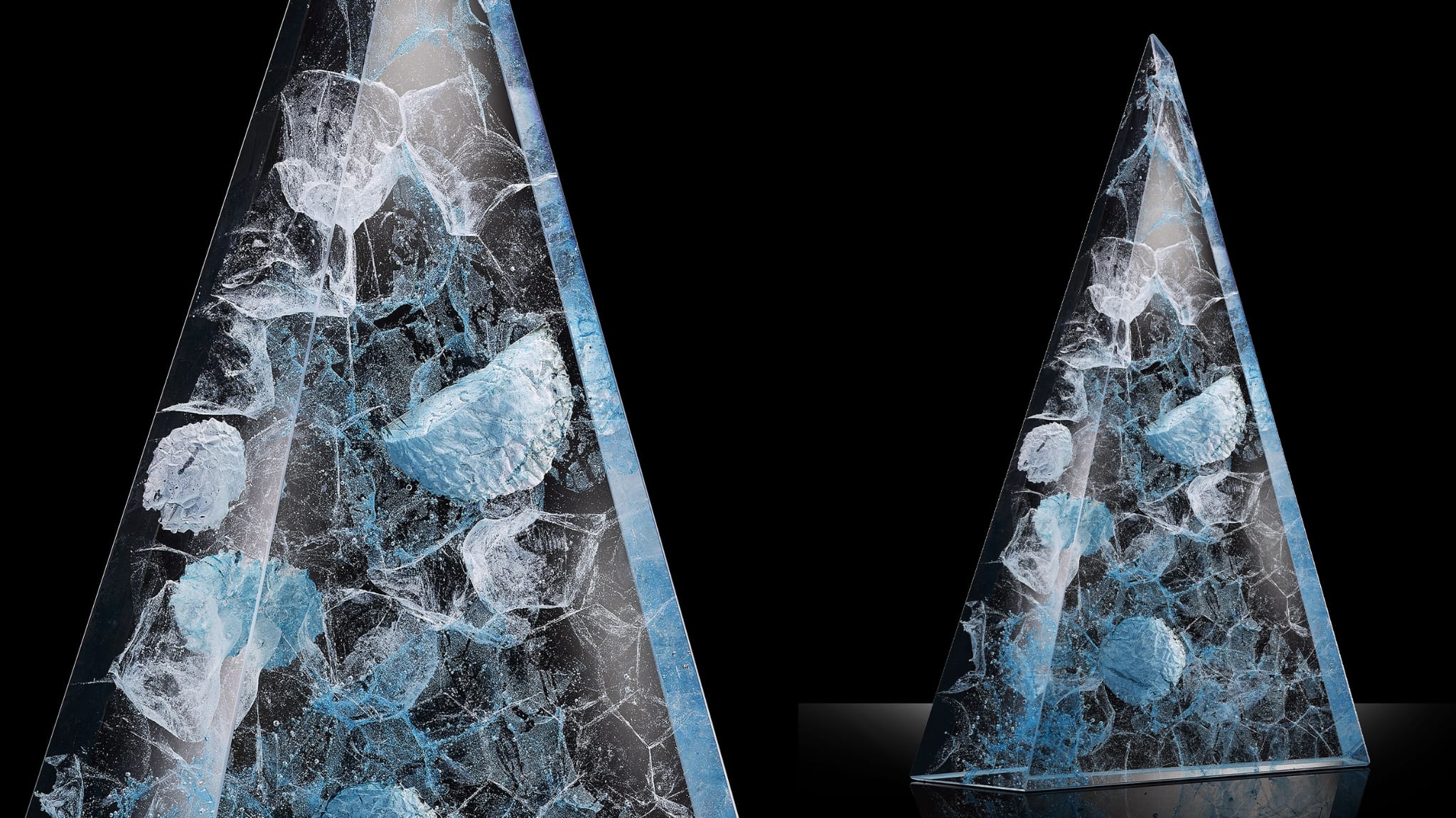 L'illustration montre deux stèles pyramidales en verre avec des formes nébuleuses, dans les tons gris-bleus. Elles se détachent du fond noir pour offrir un contraste clair-obscur.