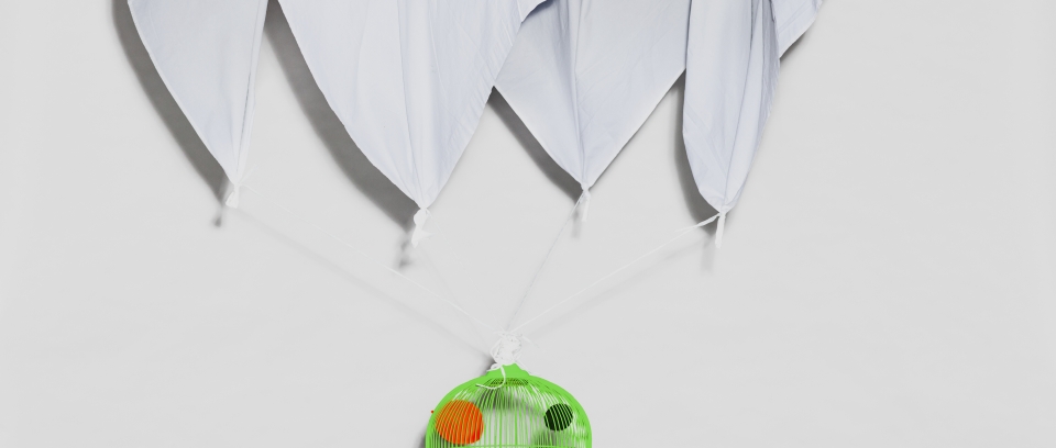L'image montre sur un fond blanc une cage d'oiseau verte fluo avec des boules de couleur dedans. Des volants en papier attachés à la cage sont tournés vers le haut