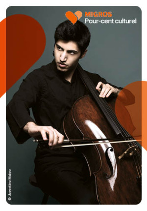 La photo montre un homme en noir assis en train de jouer du violoncelle. Il a les cheveux noirs et regarde vers sa droite quelque chose que nous ne voyons pas.