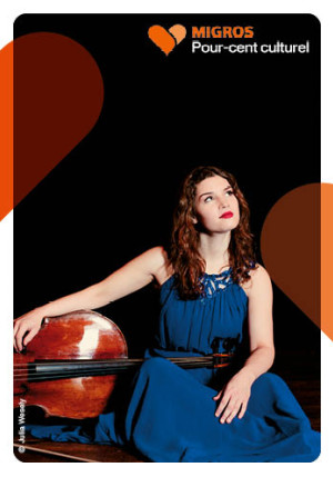 Photo de Julia Hagen par Alexandra Filippova. Julia Hagen pose avec son violoncelle. Elle est assise, une main sur son violoncelle qui est couché sur le côté. La musicienne a les cheveux roux et porte une robe bleu roi.