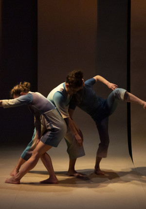 Photo prise par Elisa Murcia Artengo. Cette photo représente trois danseur-euses en mouvement sur scène. Le décor est fait de deux grands pans de papier blanc qui tombent du plafond, puis se courbent pour recouvrir le sol.